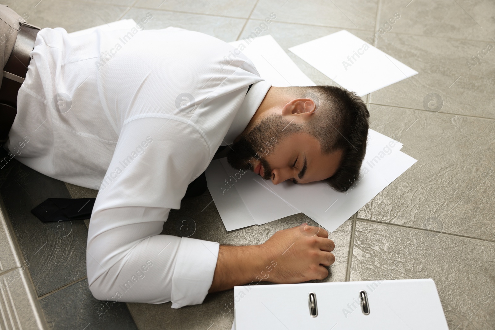 Photo of Unconscious man with scattered folder and papers lying on floor after falling down stairs indoors