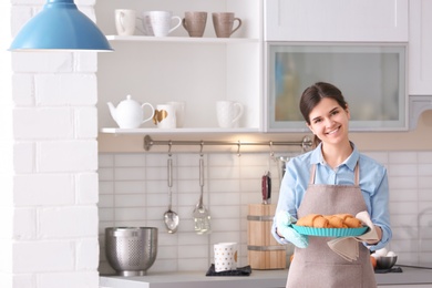 Photo of Woman holding baking dish with delicious croissants in kitchen