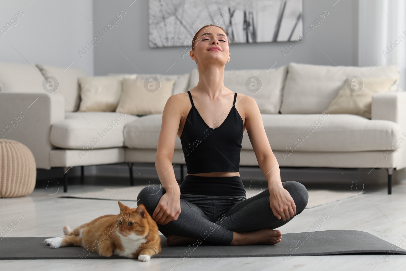 Photo of Beautiful woman with cute red cat practicing yoga on mat at home