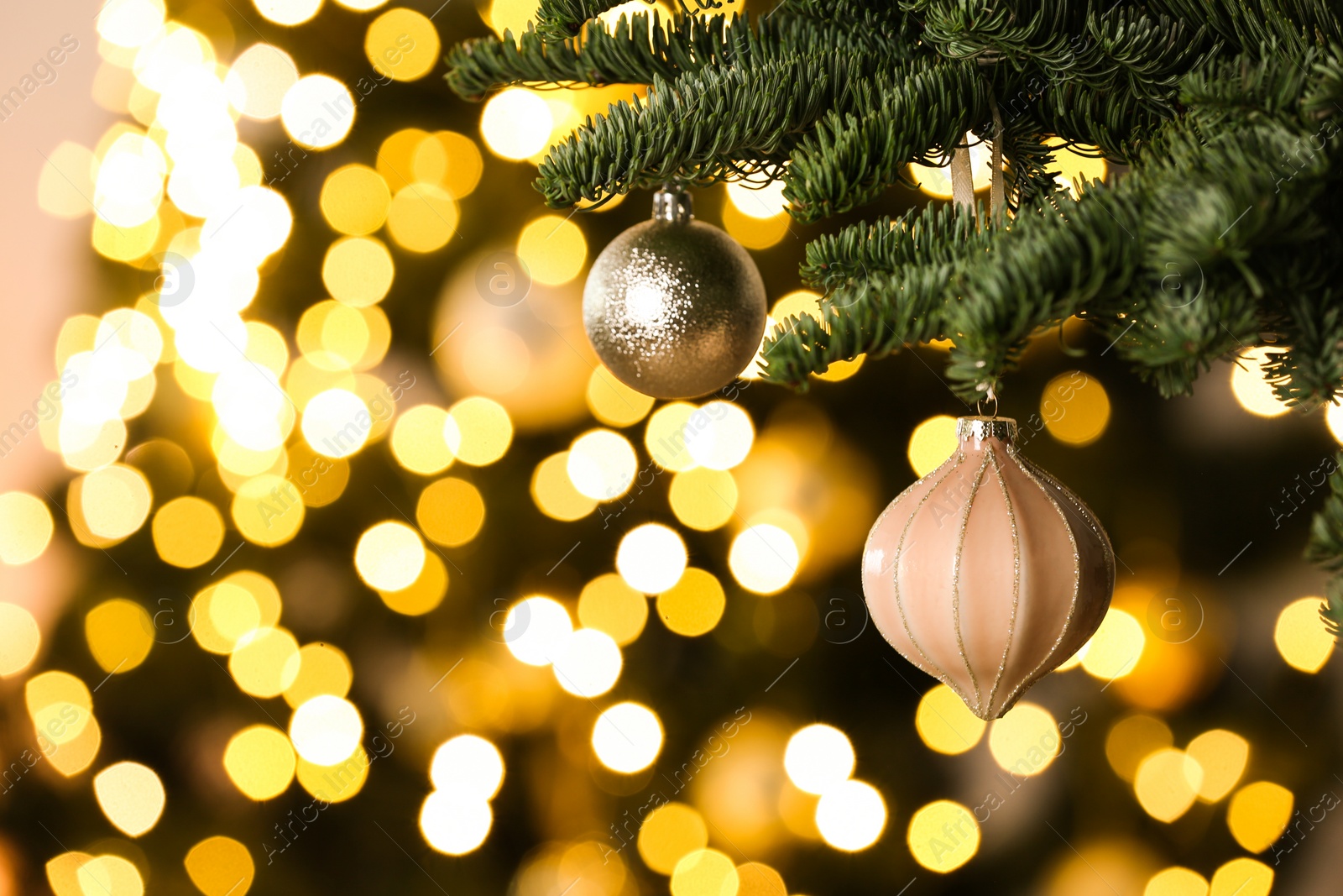 Photo of Beautiful Christmas baubles hanging on fir tree branch against blurred lights, closeup. Space for text