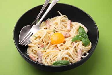 Photo of Delicious pasta Carbonara with egg yolk and cutlery on light green background, closeup