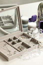 Jewelry box with many different accessories, perfumes, jars of cosmetic products and glasses on white table