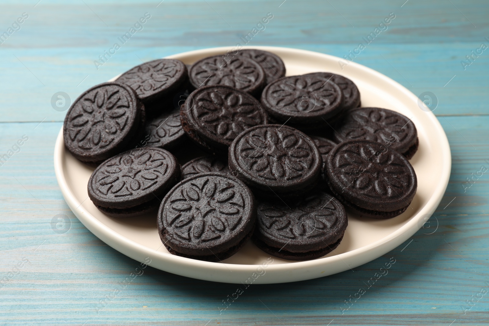 Photo of Plate with tasty sandwich cookies on light blue wooden table, closeup