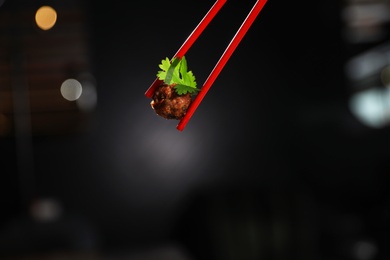 Photo of Chopsticks with meat ball on dark background, closeup. Space for text