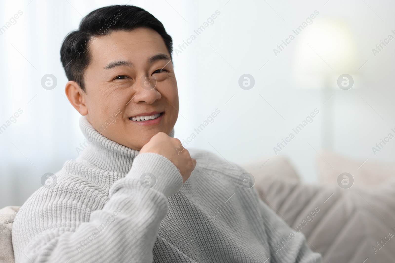 Photo of Portrait of smiling man on sofa indoors. Space for text