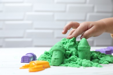 Photo of Little child playing with green kinetic sand at white table, closeup. Space for text