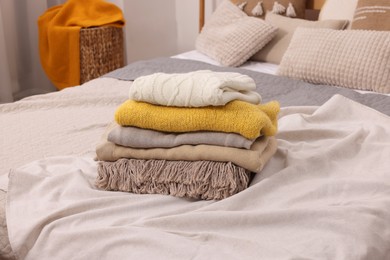 Photo of Stack of different folded blankets and clothes on bed in room. Home textile