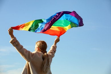 Photo of Woman holding bright LGBT flag against blue sky, back view