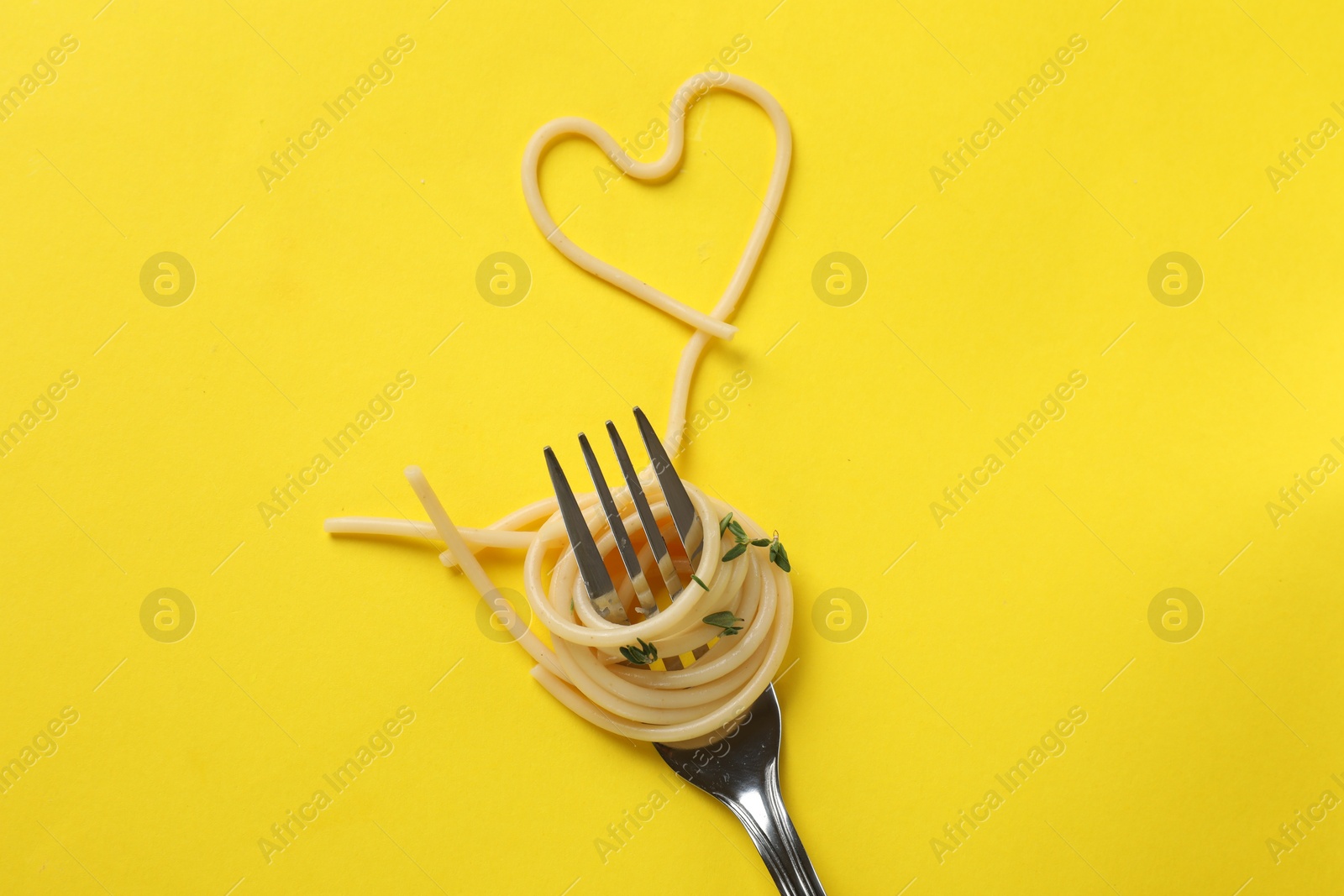 Photo of Heart made of tasty spaghetti and fork on yellow background, top view