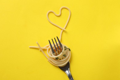 Photo of Heart made of tasty spaghetti and fork on yellow background, top view