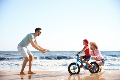 Photo of Happy parents teaching son to ride bicycle on sandy beach near sea
