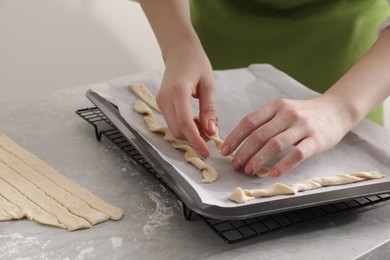 Woman putting homemade breadsticks on baking sheet at light grey marble table, closeup. Cooking traditional grissini