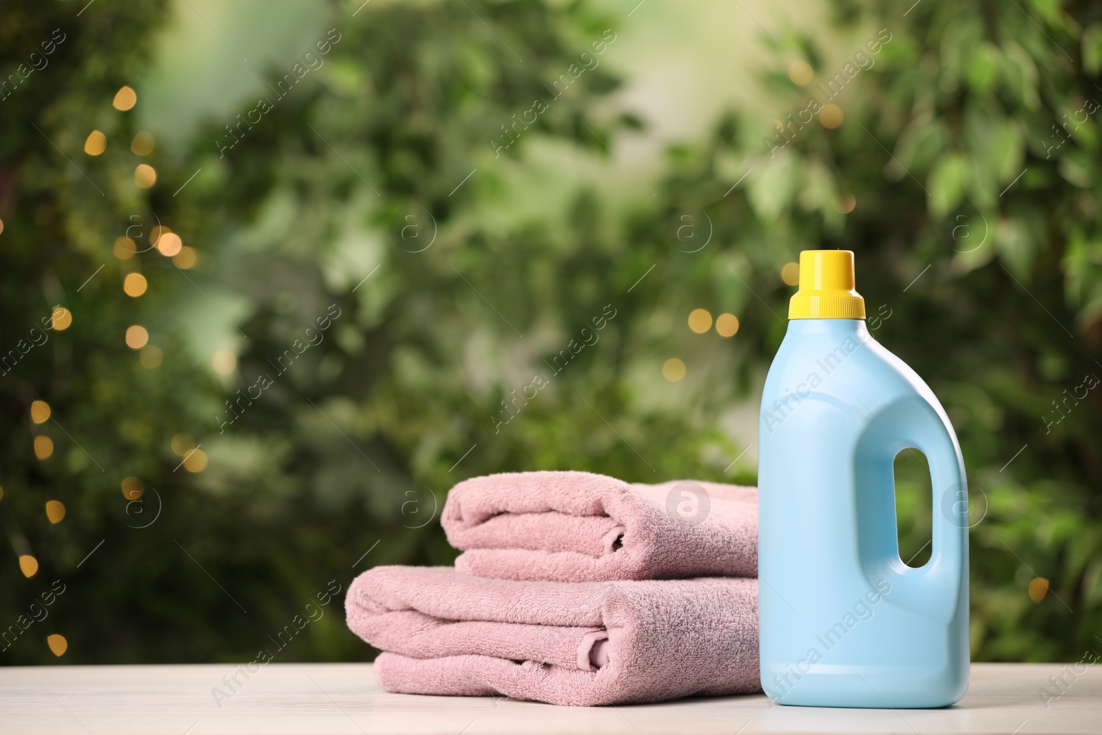 Photo of Detergent and clean towels on white wooden table outdoors, space for text. Laundry day