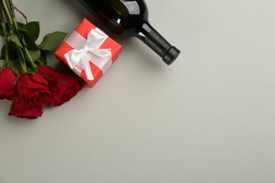 Photo of Beautiful gift box, roses and wine on grey background, flat lay with space for text. Valentine's day celebration