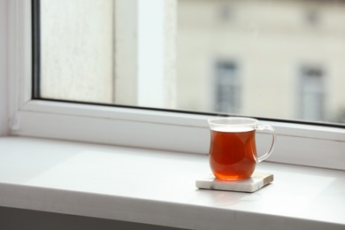 Photo of Cup of hot tea on white sill near window. Space for text