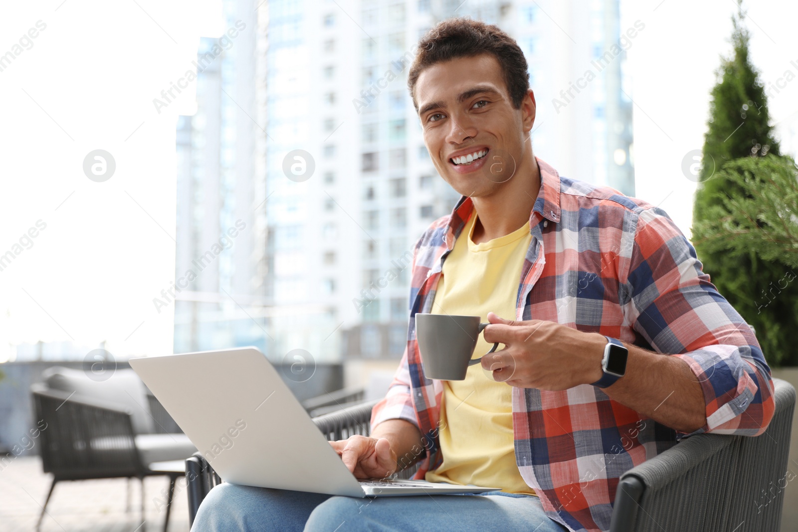 Photo of Portrait of handsome young African-American man with laptop and cup of drink in outdoor cafe