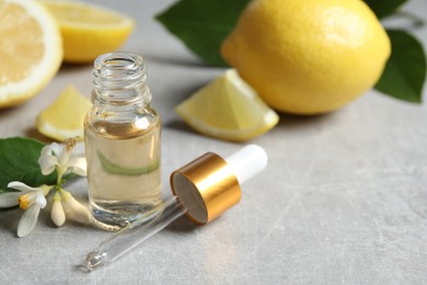 Photo of Citrus essential oil, flower and lemons on light table. Space for text