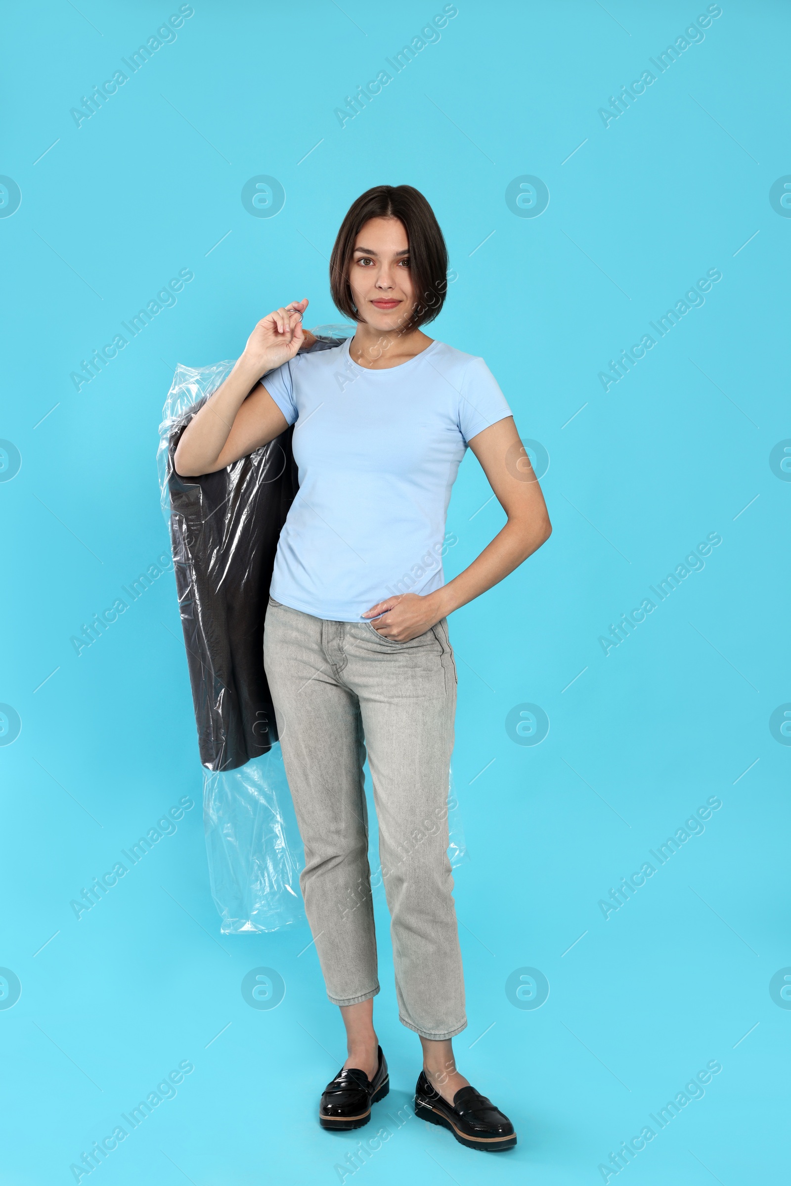 Photo of Woman holding garment cover with clothes on light blue background. Dry-cleaning service