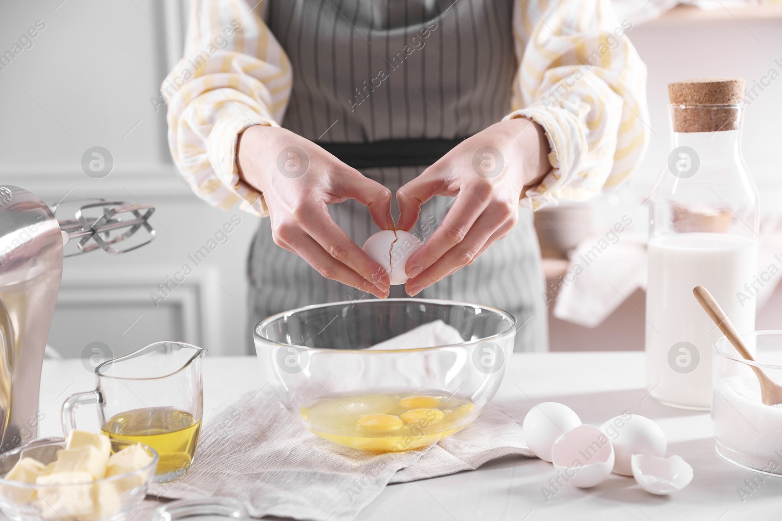 Photo of Making dough. Woman breaking egg at white table in kitchen, closeup