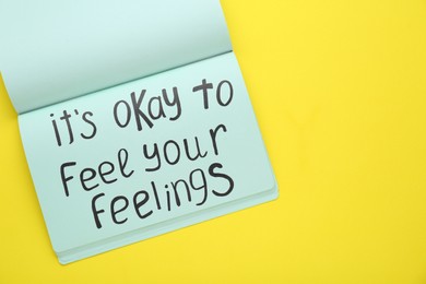 Notebook with phrase It`s Okay To Feel Your Feelings on yellow background, top view. Space for text