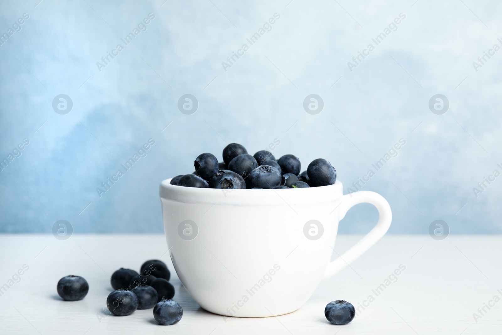 Photo of Fresh ripe blueberries in cup on white wooden table