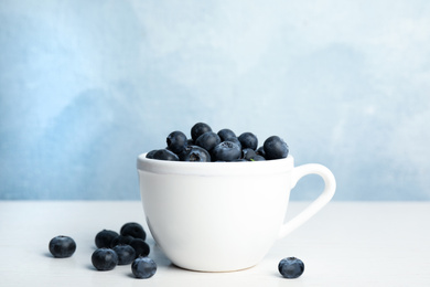 Fresh ripe blueberries in cup on white wooden table