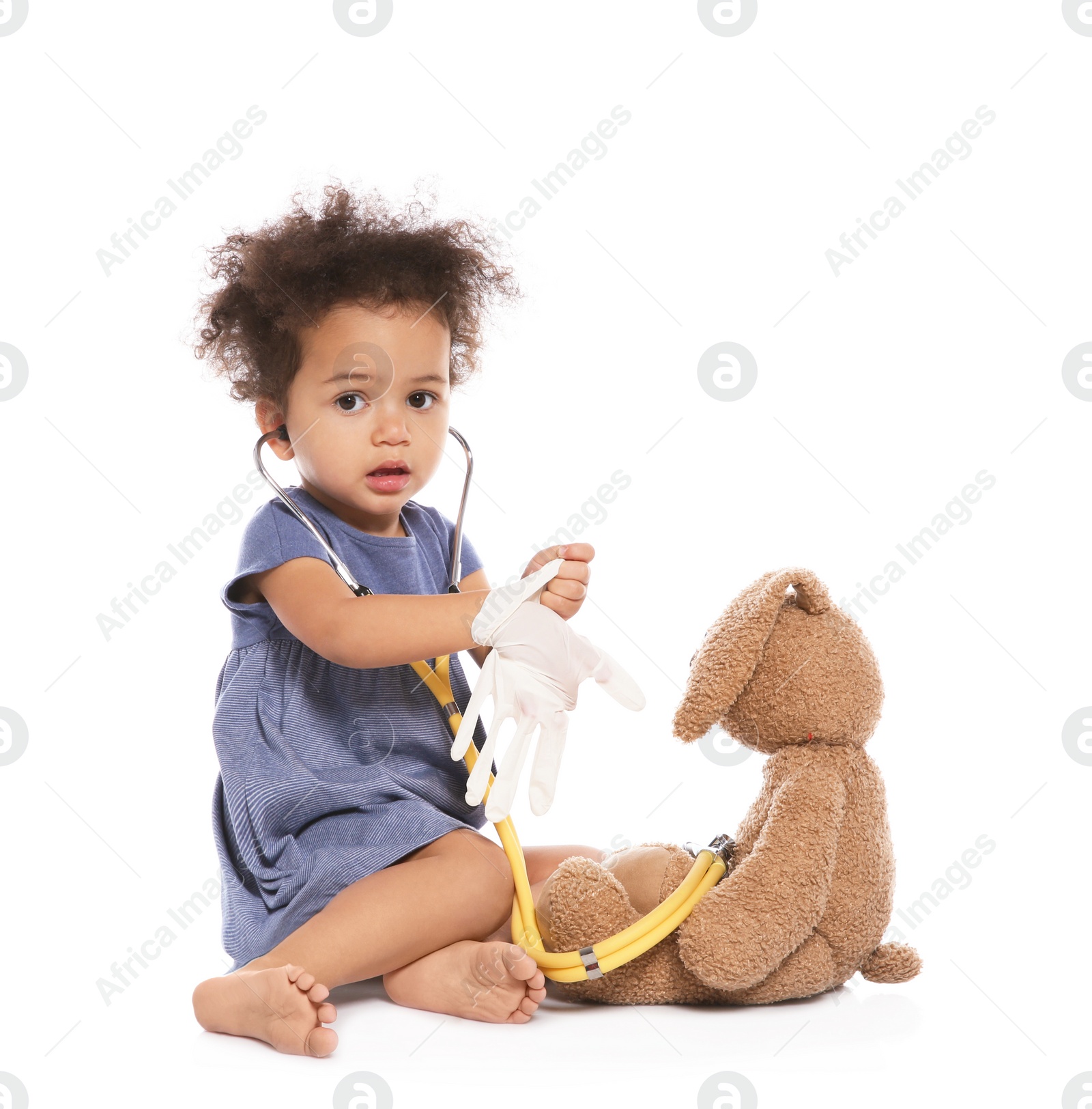 Photo of Cute African American child imagining herself as doctor while playing with stethoscope and toy bunny on white background