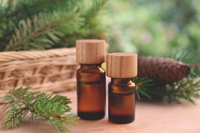 Photo of Bottles of pine essential oil, cone and branches on wooden table, closeup