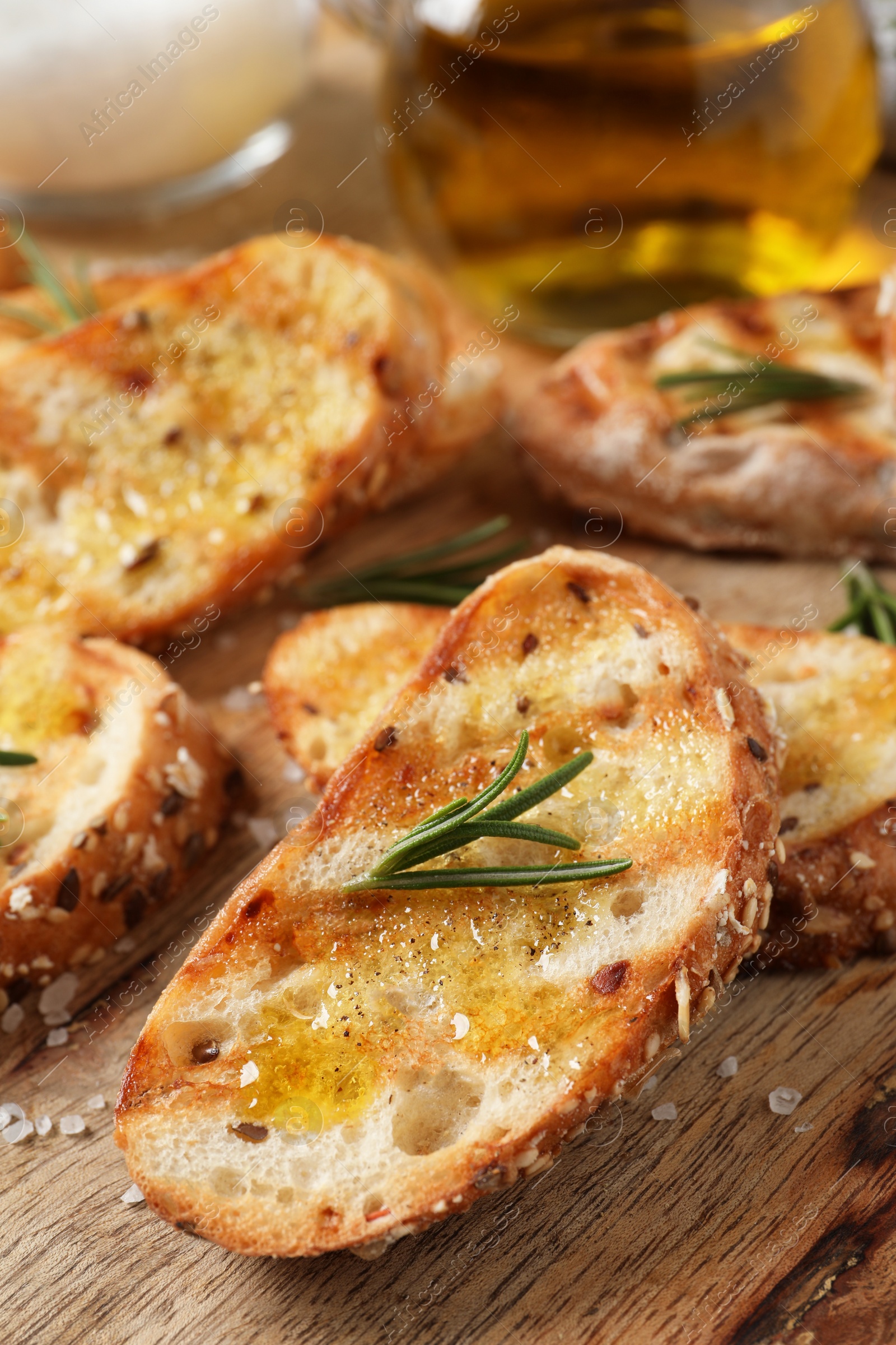 Photo of Tasty bruschettas with oil and rosemary on wooden board, closeup