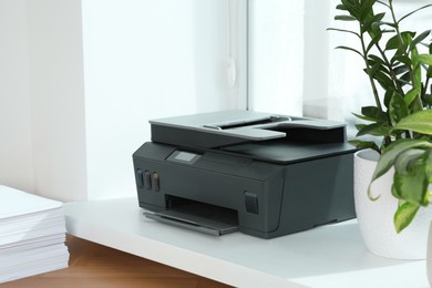 Photo of Stack of paper on wooden table near window sill with modern printer in office