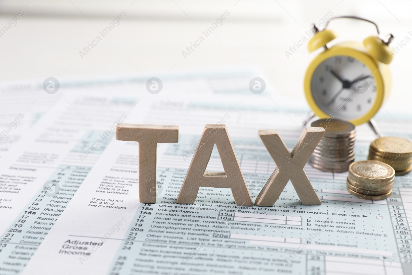 Photo of Word Tax made with wooden letters, documents, coins and alarm clock on light table