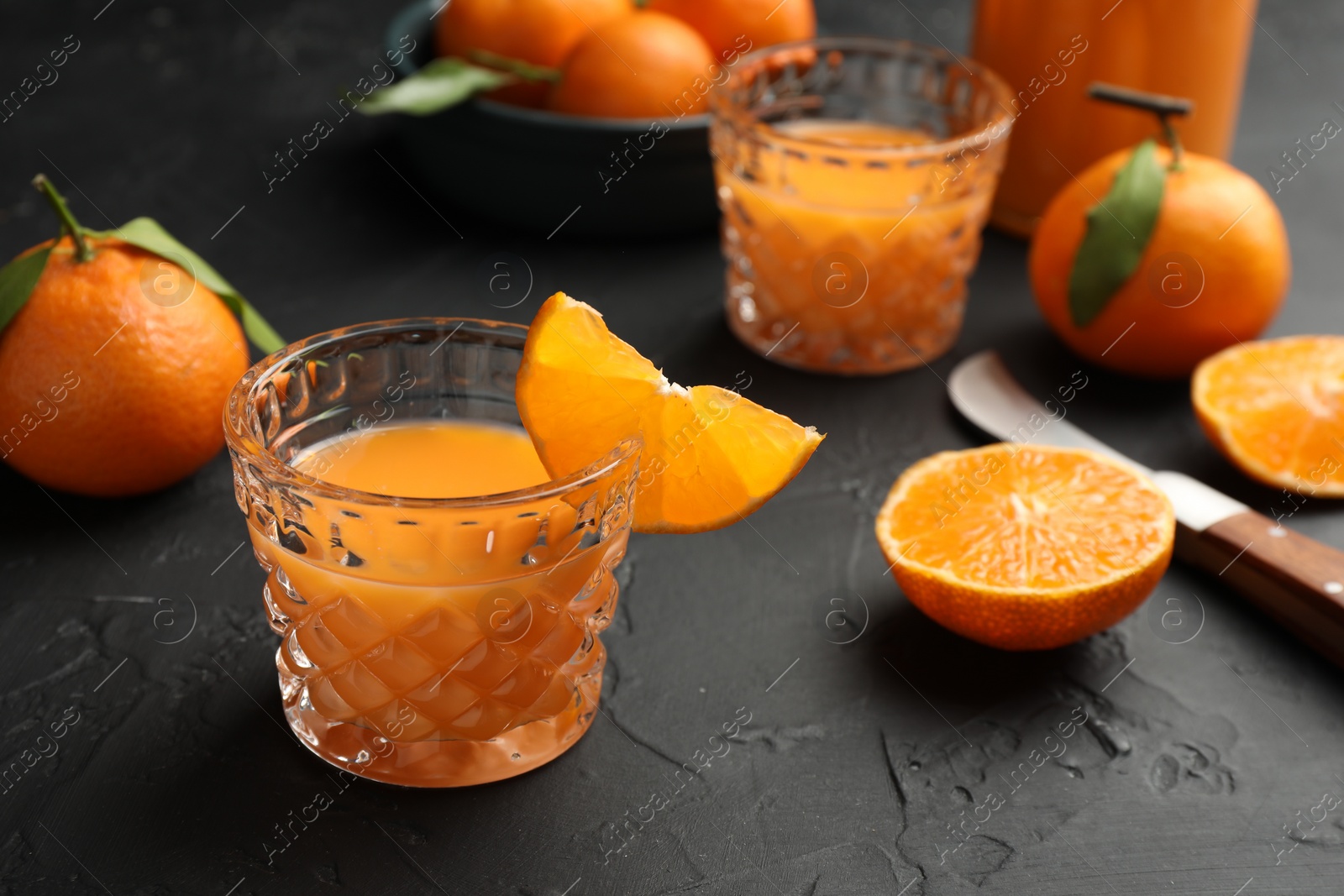 Photo of Tasty tangerine liqueur in glasses and fresh citrus fruits on black textured table