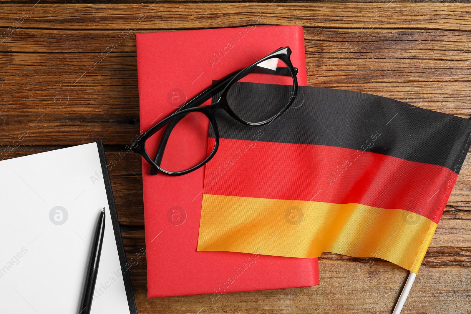 Photo of Learning foreign language. Flag of Germany, book, glasses and stationery on wooden table, flat lay