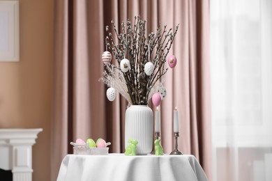 Photo of Pussy willow branches with festively decorated eggs, Easter bunnies and burning candles on table at home