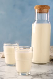 Photo of Carafe and glass of fresh milk on white marble table