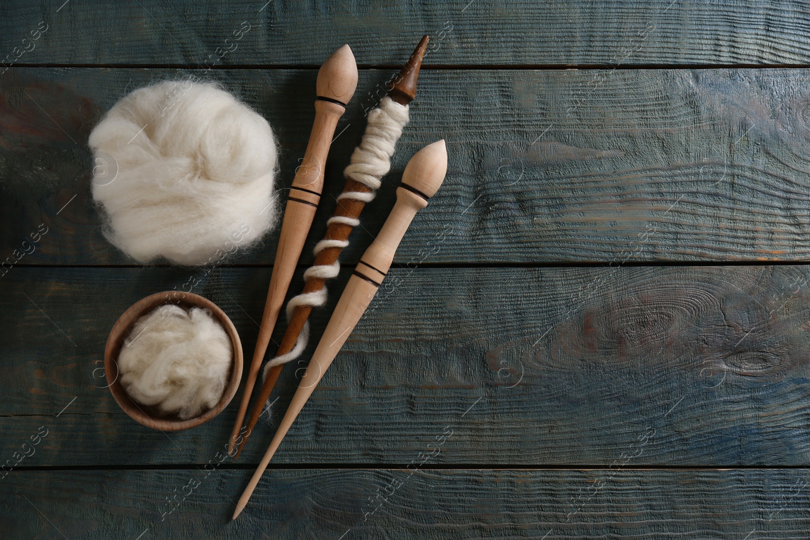 Photo of Soft white wool and spindles on blue wooden table, flat lay. Space for text