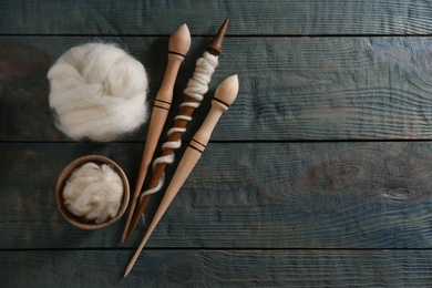 Soft white wool and spindles on blue wooden table, flat lay. Space for text