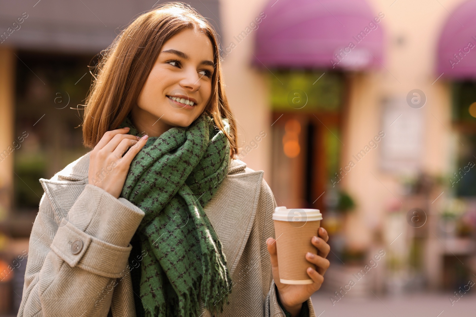 Photo of Beautiful woman in warm scarf with paper cup of coffee on city street, space for text