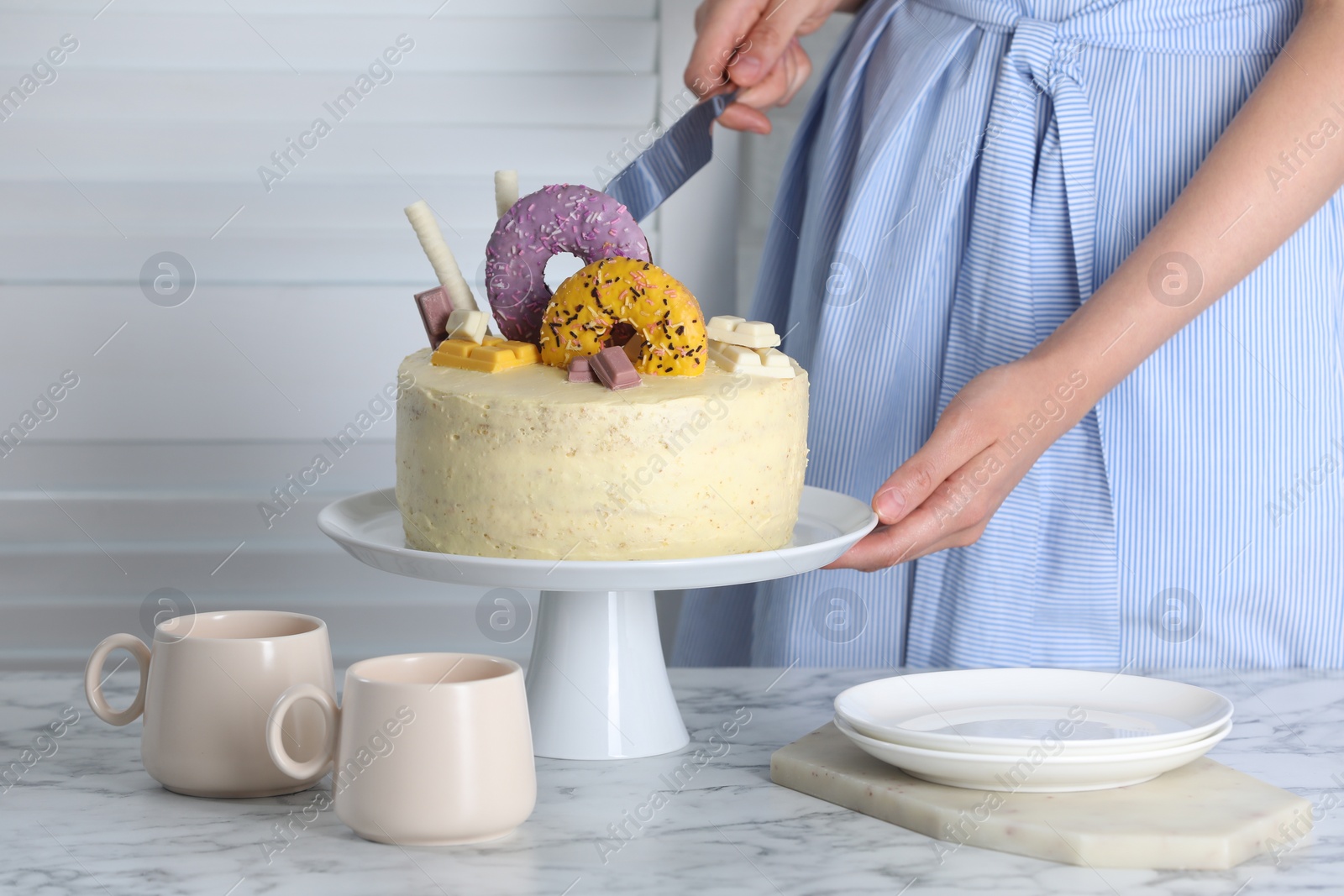 Photo of Woman cutting delicious cake decorated with sweets at white marble table, closeup