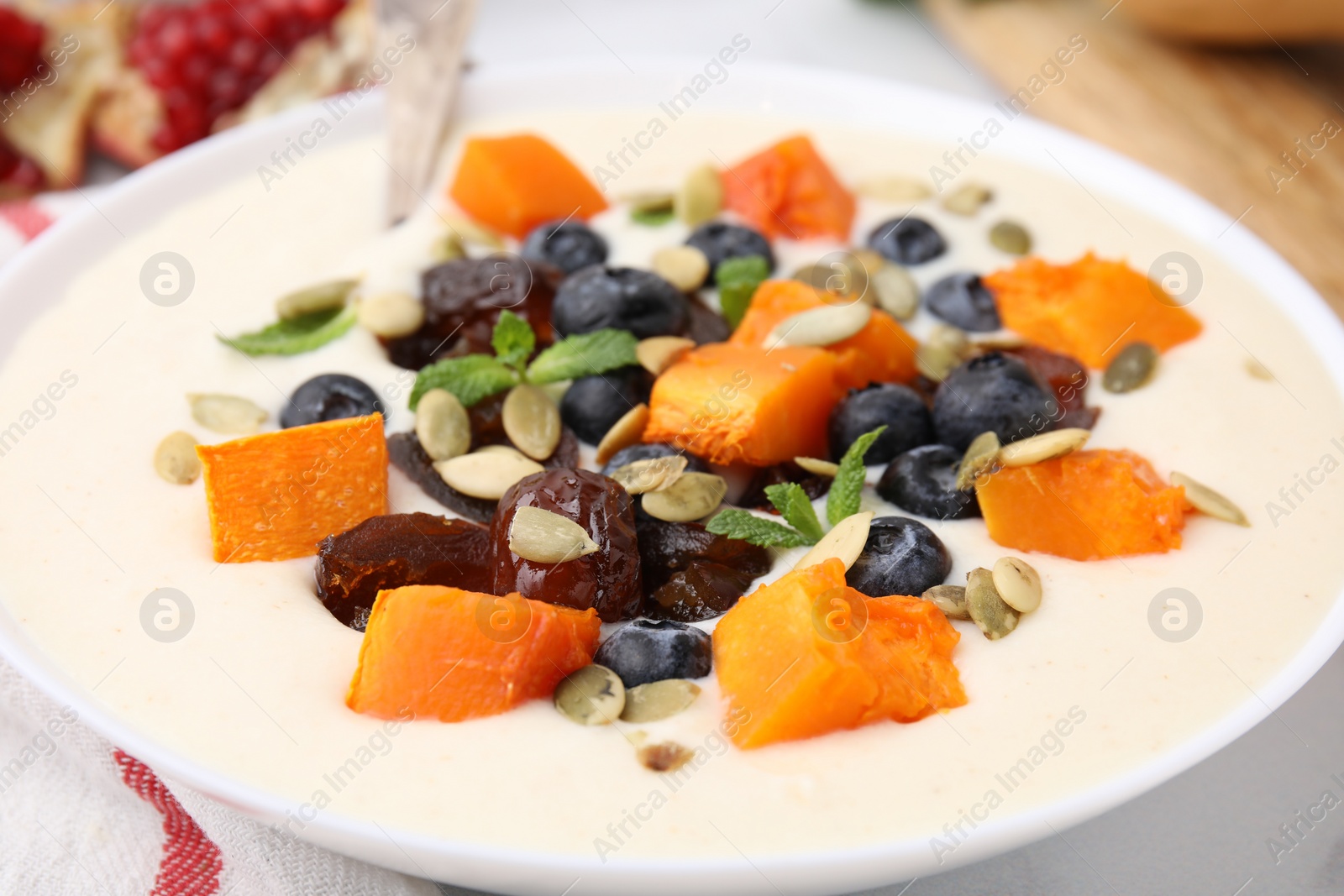 Photo of Delicious semolina pudding with blueberries, dates, pumpkin and mint in bowl on table, closeup