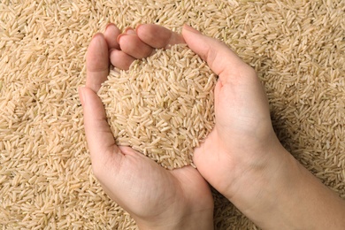 Photo of Woman holding heap of cereal over raw brown rice