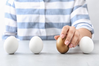 Woman choosing golden egg from white ones at table, closeup