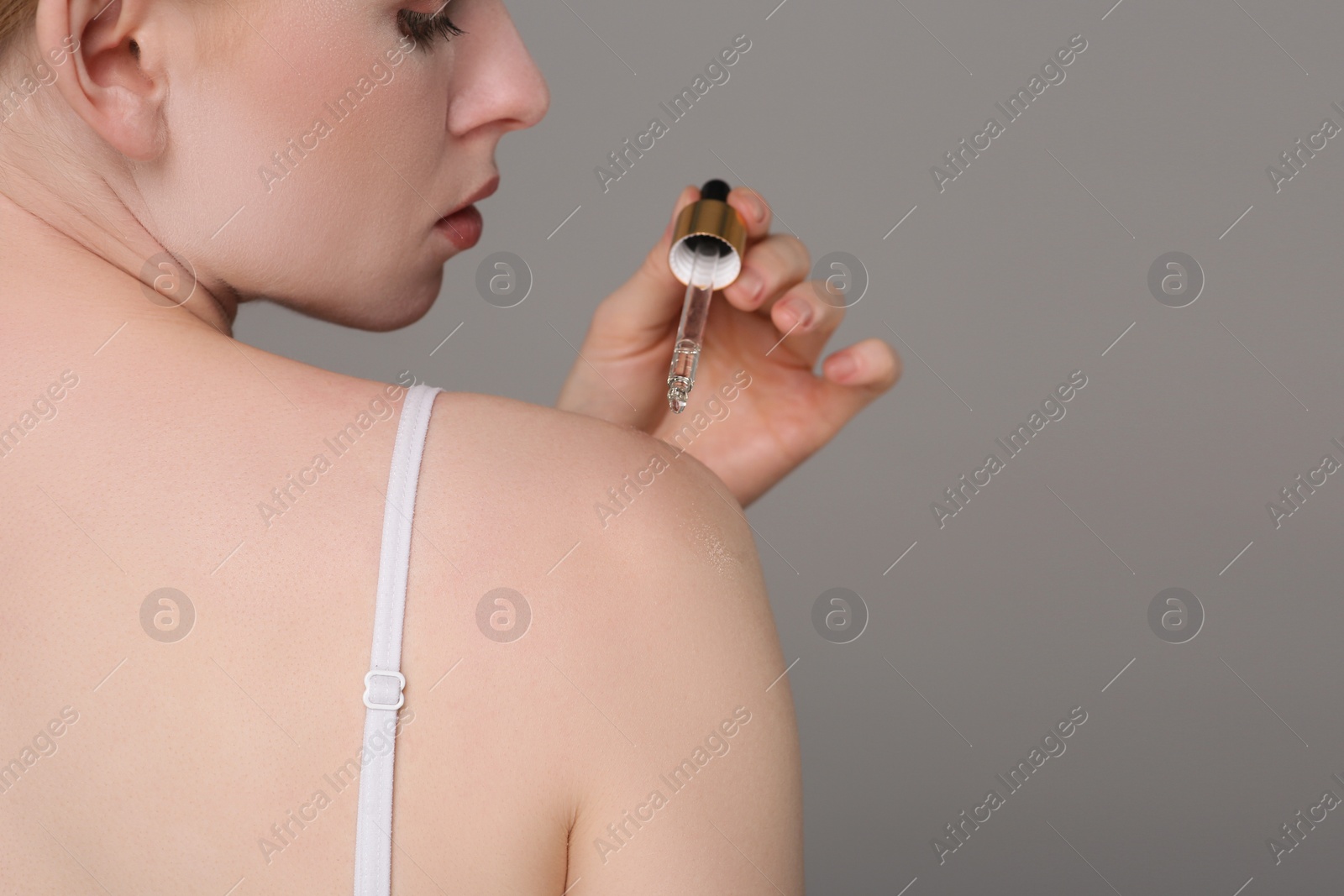 Photo of Woman applying essential oil onto shoulder on grey background, closeup. Space for text