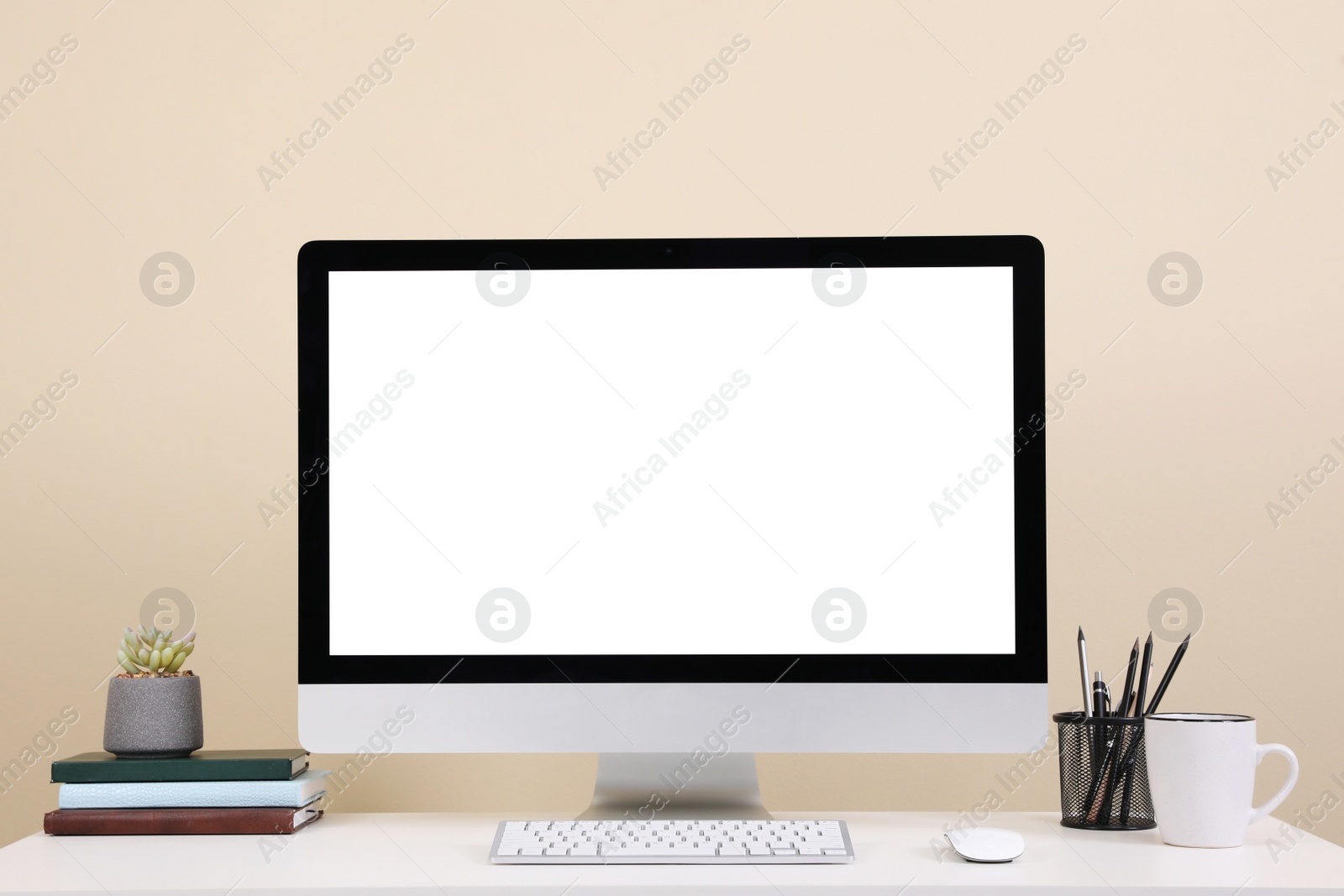 Photo of Comfortable workplace with blank computer display on desk near beige wall. Space for text