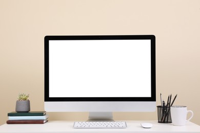 Comfortable workplace with blank computer display on desk near beige wall. Space for text