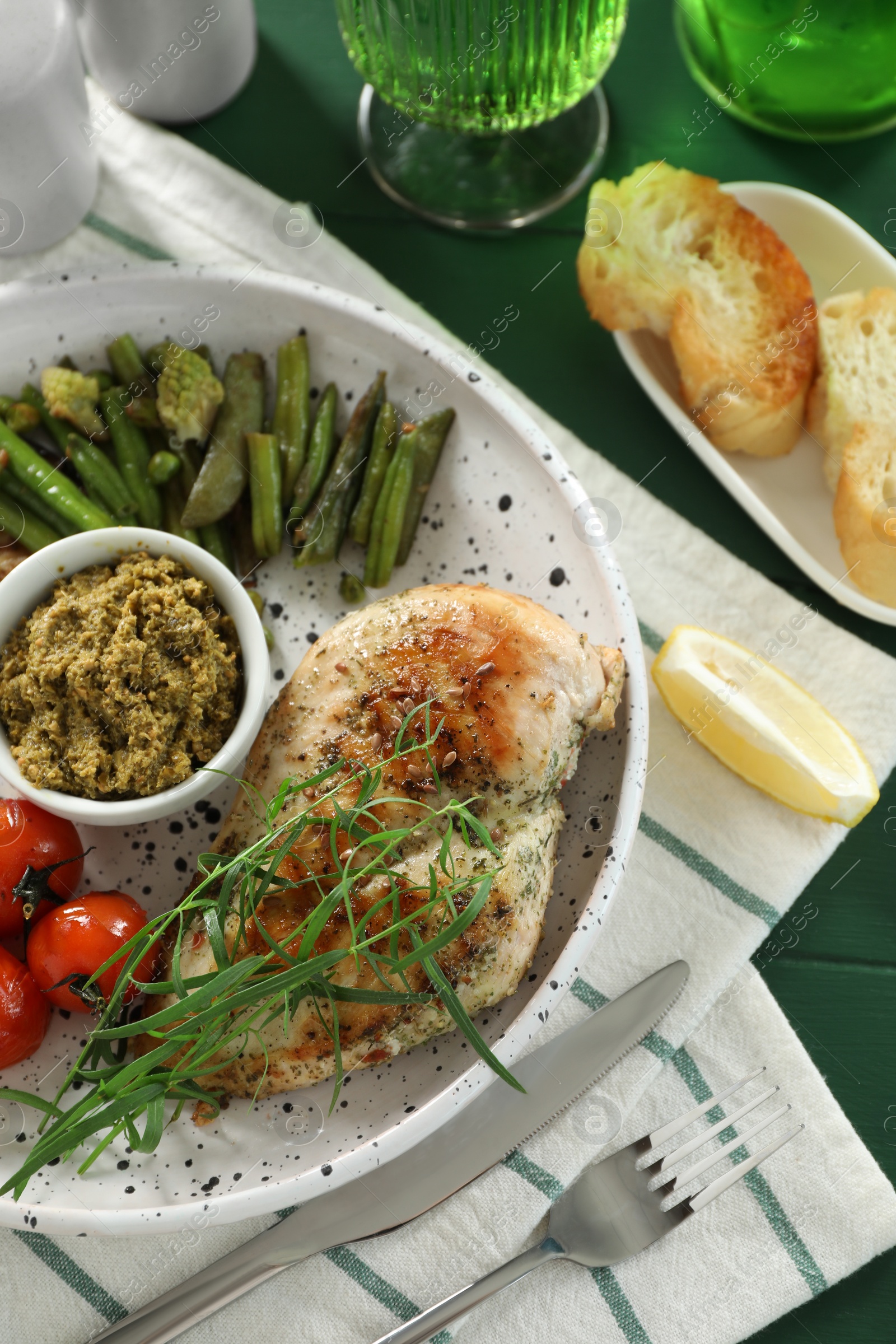 Photo of Tasty chicken, vegetables with tarragon and pesto sauce served on green table, above view