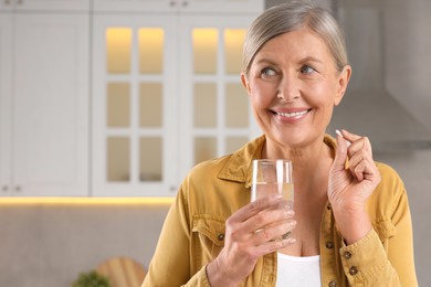 Photo of Menopause, hormone replacement therapy. Happy woman holding glass of water and pill in kitchen, space for text