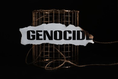 Photo of Paper with word Genocide and golden cage on black background