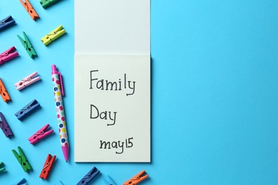 Photo of Notebook with text Family Day May 15, pen and decorative clothespins on light blue background, flat lay. Space for design