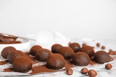 Photo of Delicious chocolate truffles with cocoa powder and hazelnuts on white marble table, space for text